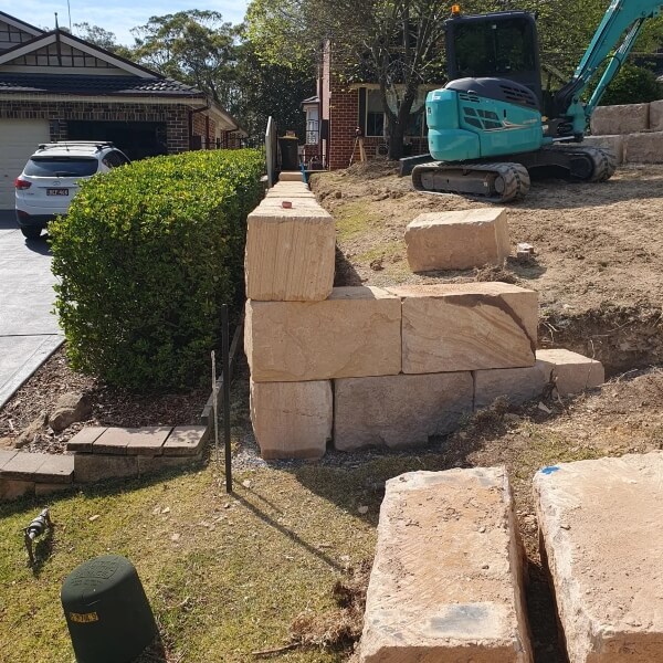 Sandstone block retaining wall construction in Western Sydney with excavator preparing residential sloped yard by West Sydney Landscapes